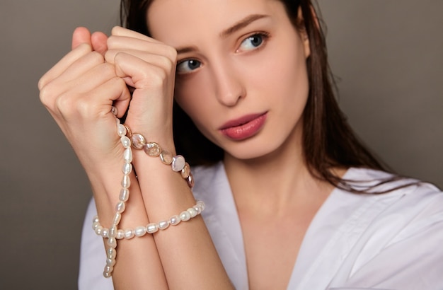 Portrait de beauté de femme avec une chemise blanche et un collier autour de ses mains sur fond marron