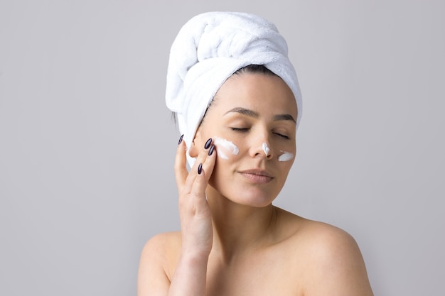 Portrait de beauté de femme dans une serviette blanche sur la tête applique de la crème sur le visage Nettoyage de soins de la peau eco