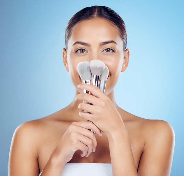 Portrait beauté et femme avec des pinceaux de maquillage en studio isolé sur fond bleu Cosmétiques pour le visage et modèle féminin avec fond de teint pour le visage ou pinceau à poudre pour l'esthétique et le bien-être