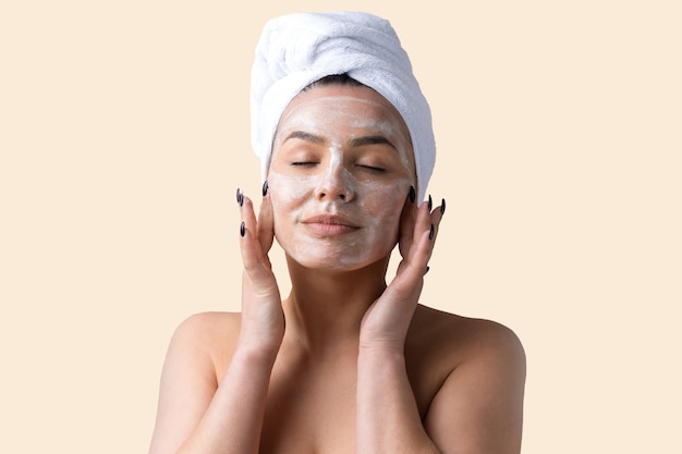 Portrait de beauté de femme en serviette blanche sur la tête applique de la crème sur le visage. Soins de la peau nettoyant le concept de détente du spa cosmétique bio écologique.