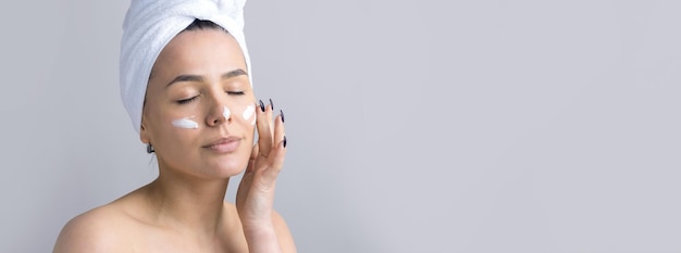 Portrait de beauté d'une femme en serviette blanche sur la tête applique de la crème sur le visage