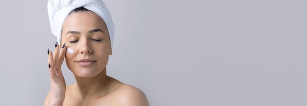 Portrait de beauté d'une femme en serviette blanche sur la tête applique de la crème sur le visage