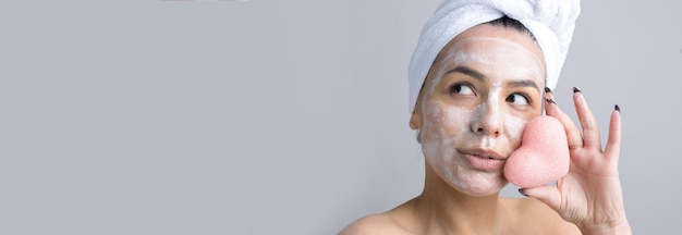 Portrait de beauté de femme en serviette blanche sur la tête avec une éponge pour un corps en vue d'un coeur rose