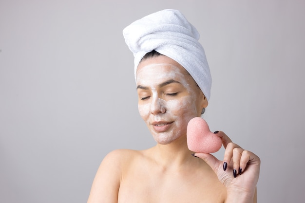 Portrait de beauté de femme en serviette blanche sur la tête avec une éponge pour un corps en vue d'un coeur rose