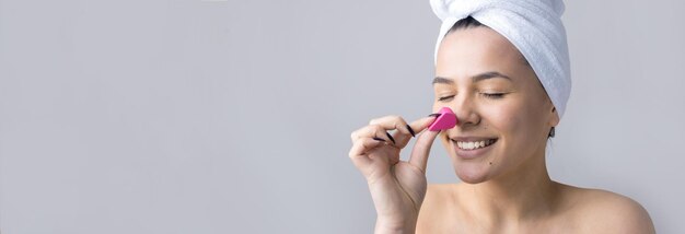 Portrait de beauté d'une femme en serviette blanche sur la tête avec une éponge pour un corps en vue d'un coeur rose