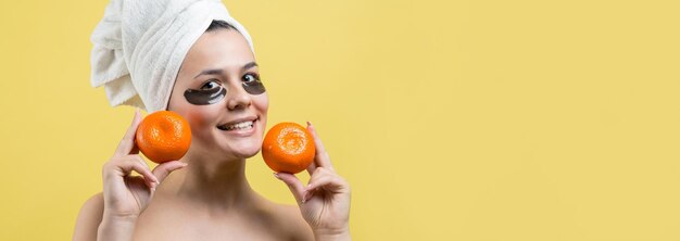 Portrait de beauté d'une femme en serviette blanche sur la tête avec un masque nourrissant doré sur le visage Soins de la peau nettoyant le spa cosmétique bio bio concept de détente Une fille se tient le dos tenant une mandarine orange