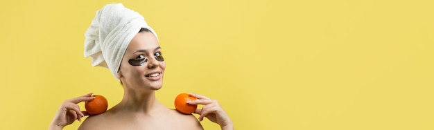 Portrait de beauté d'une femme en serviette blanche sur la tête avec un masque nourrissant doré sur le visage Soins de la peau nettoyant le spa cosmétique bio bio concept de détente Une fille se tient le dos tenant une mandarine orange