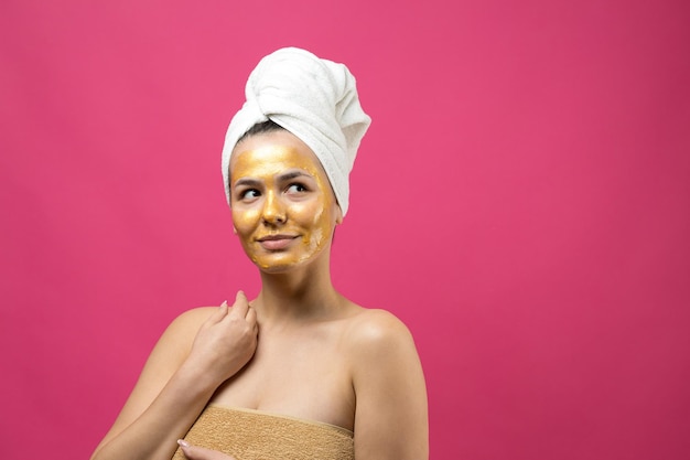 Portrait de beauté d'une femme en serviette blanche sur la tête avec un masque nourrissant doré sur le visage