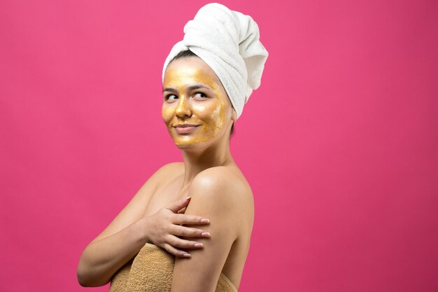 Portrait de beauté d'une femme en serviette blanche sur la tête avec un masque nourrissant doré sur le visage