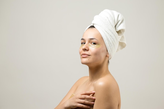 Portrait de beauté d'une femme en serviette blanche sur la tête avec un masque nourrissant doré sur le visage