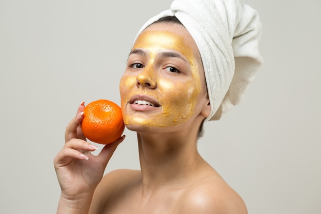 Portrait de beauté d'une femme en serviette blanche sur la tête avec un masque nourrissant doré sur le visage