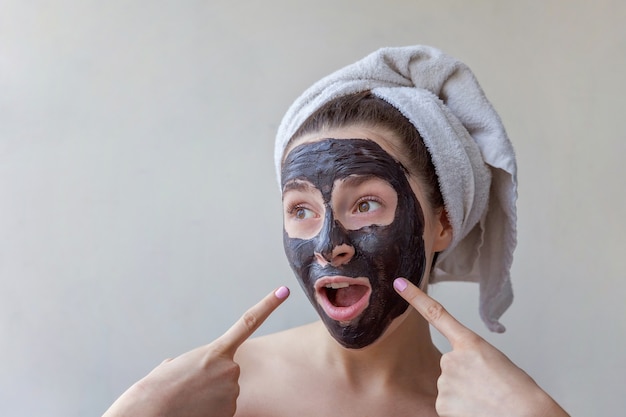 Portrait de beauté de femme en serviette sur la tête, appliquer un masque nourrissant noir sur le visage