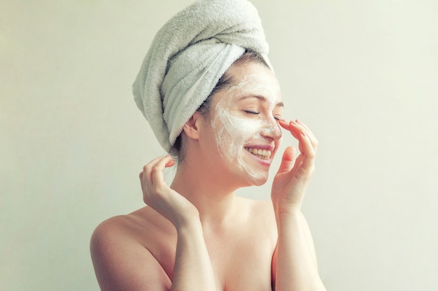 Portrait de beauté de femme en serviette sur la tête avec masque nourrissant blanc ou crème sur le visage, fond blanc isolé. Concept de détente de spa cosmétique bio écologique pour le nettoyage des soins de la peau