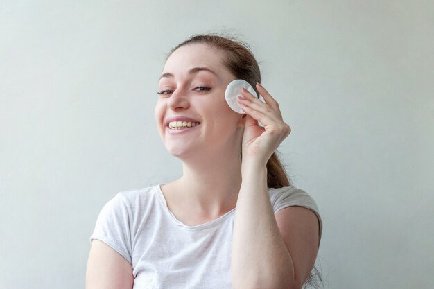 Portrait de beauté de femme souriante avec une peau douce et saine enlever le maquillage avec un coton isolé sur fond blanc.