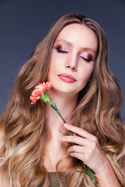 Portrait de beauté d'une fille Une belle femme touche son visage avec une fleur d'oeillet Soins du visage Cosmétologie soins de la peau et spa