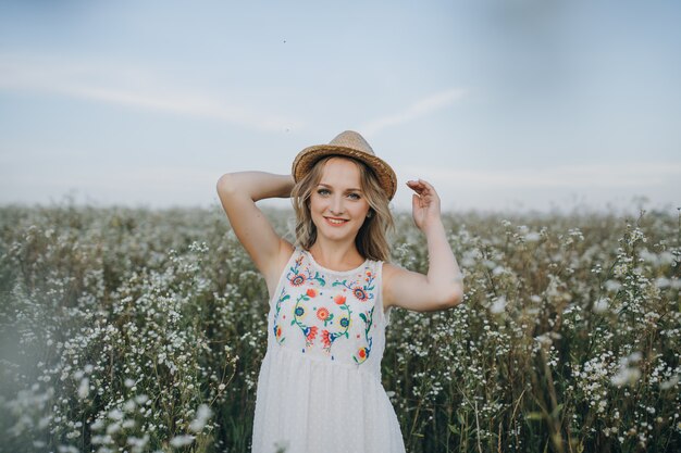 Portrait de beauté fille avec un chapeau à la main marche dans un champ avec des fleurs des champs et sourit sincèrement