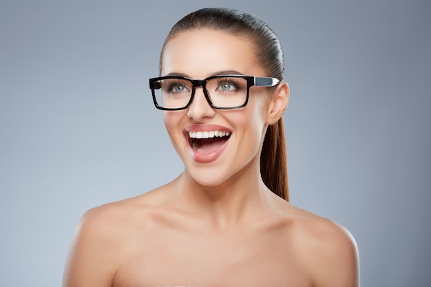 Portrait de beauté d'une fille souriante heureuse dans des verres à la recherche de côté Tête et épaules de belle femme souriant gaiement largement. Maquillage naturel, studio, vraies émotions