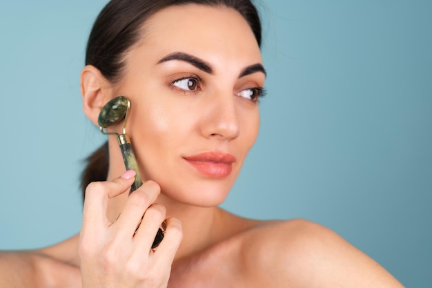 Portrait de beauté en gros plan d'une femme avec une peau parfaite et un maquillage naturel, des lèvres nues charnues, tenant un masseur à rouleaux pour le visage et le cou