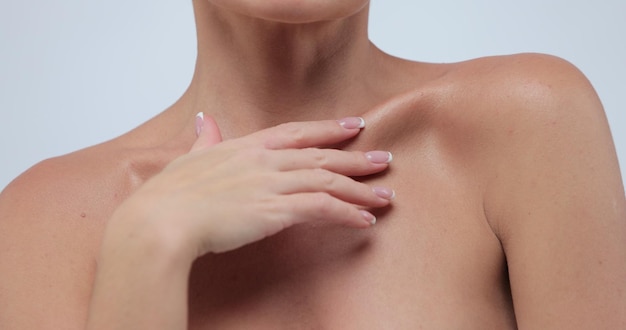 Portrait de beauté en gros plan d'une jeune femme à la peau lisse et saine caresse sa peau au niveau de la clavicule sur fond gris