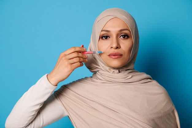 Portrait de beauté isolé d'une jeune femme musulmane arabe tenant une seringue près de son visage.