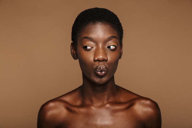 Portrait de beauté d'une jeune femme africaine à moitié nue aux cheveux noirs courts isolé sur beige