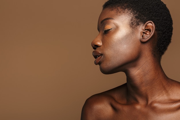 Portrait de beauté d'une jeune femme africaine à moitié nue aux cheveux noirs courts isolé sur beige