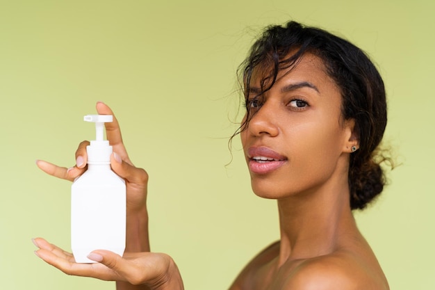 Portrait de beauté d'une jeune femme afro-américaine topless aux épaules nues sur fond vert avec une bouteille blanche de lotion pour le corps