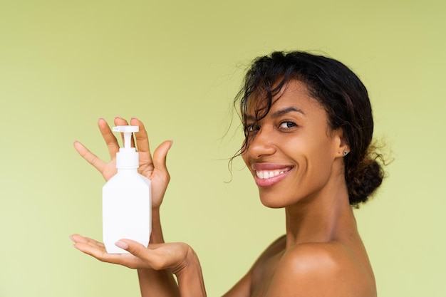 Portrait de beauté d'une jeune femme afro-américaine topless aux épaules nues sur fond vert avec une bouteille blanche de lotion pour le corps