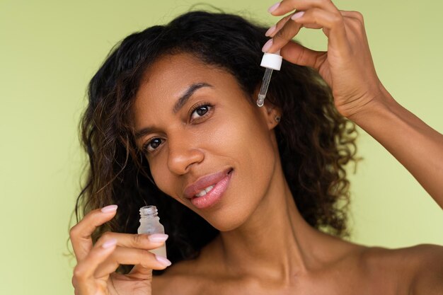 Portrait de beauté d'une jeune femme afro-américaine topless aux épaules nues sur fond vert avec une peau parfaite contient du sérum pour la jeunesse et l'hydratation de la peau