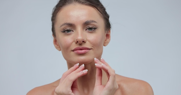 Portrait de beauté d'une jeune femme à la peau lisse et saine, elle touche doucement son visage avec ses doigts sur fond gris