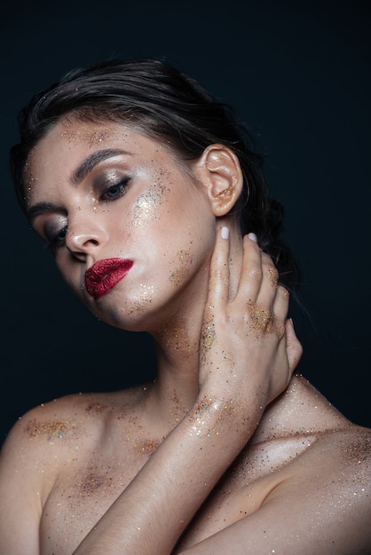 Portrait de beauté d'une jeune femme sensuelle avec un maquillage brillant et brillant touchant son cou sur une surface noire