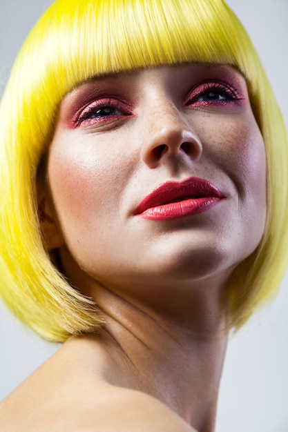 Portrait de beauté d'une jeune mannequin calme et mignonne avec des taches de rousseur, du maquillage rouge et une perruque jaune. tourné en studio intérieur, isolé sur fond gris.