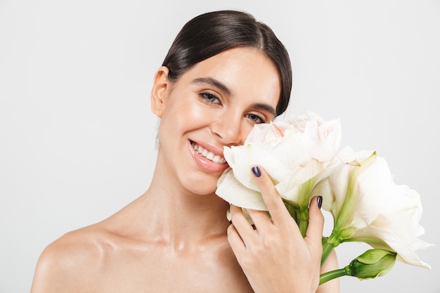 Portrait de beauté d'une jolie femme en bonne santé sensuelle debout isolé sur un mur blanc, posant avec une fleur