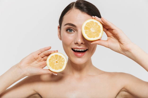 Portrait de beauté d'une jolie jeune femme aux seins nus isolée sur un mur blanc, montrant du citron tranché