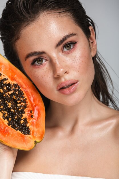 Portrait de beauté d'une jolie jeune femme brune debout isolé sur blanc, posant avec papaye