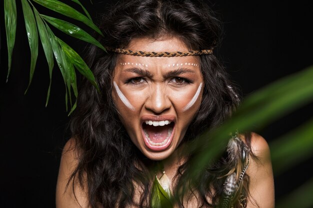 Portrait de beauté d'une jolie jeune femme brune portant des accessoires tribaux posant avec des feuilles tropicales isolées, criant