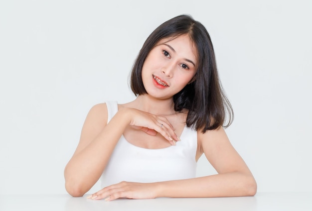 Portrait de beauté tourné, gros plan d'un modèle de cheveux noirs courts asiatiques millénaires avec maquillage lèvre rouge en maillot de corps assis à table posant regarder la caméra sur fond blanc.