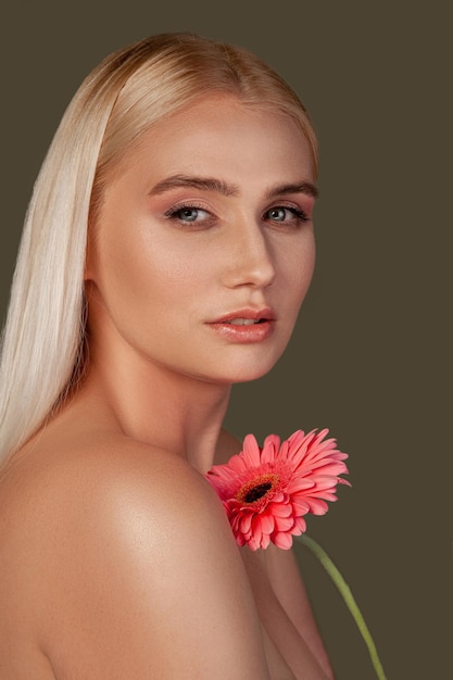 Portrait de beauté traitement ayurvédique femme blonde à la peau lisse fleur de marguerite gerber rose isolée sur marron