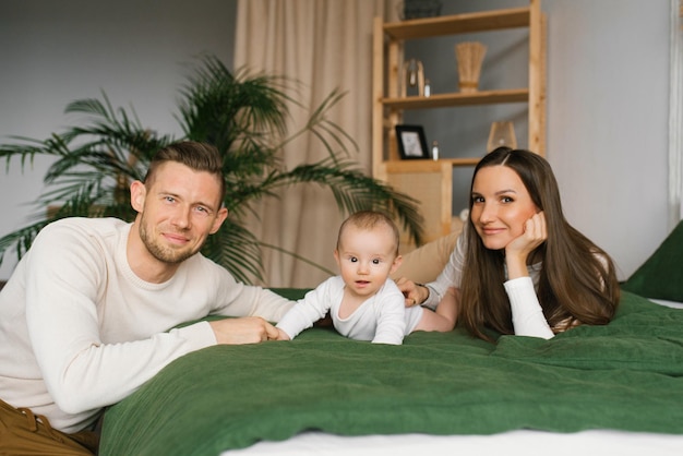 Portrait de beaux jeunes parents et d'un enfant mignon regardant dans la caméra et souriant couché ensemble dans son lit sur le ventre