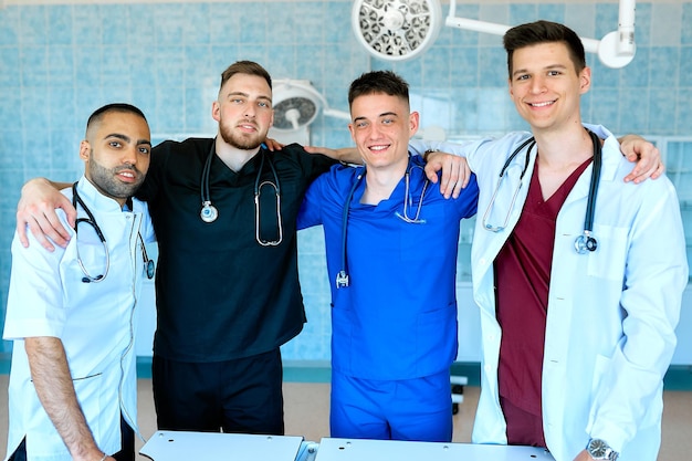 Un portrait de beaux médecins masculins souriants portant des gommages et tenant des stéthoscopes dans un cabinet médical.