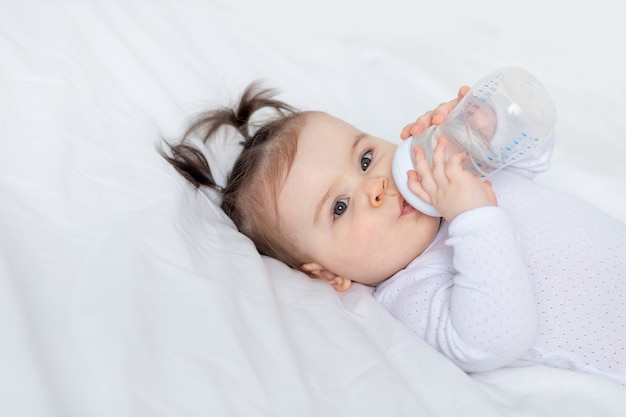 Portrait d'un bébé avec une bouteille sur le lit à la maison, concept de nourriture pour bébé