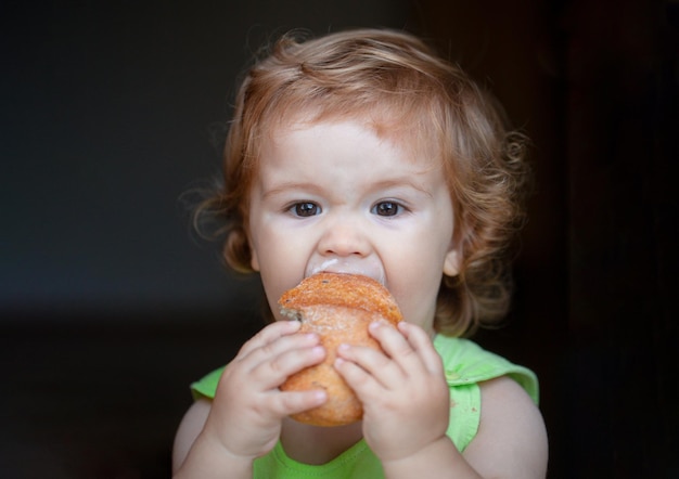 Portrait d'un bébé drôle avec du pain dans ses mains en train de manger