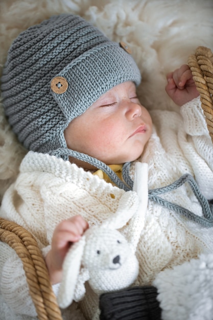 Portrait d'un bébé endormi dans un bonnet tricoté chaud avec un jouet tricoté dans la poignée se bouchent.