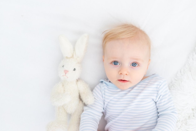 Portrait d'un bébé garçon blond de six mois sur un lit avec un jouet