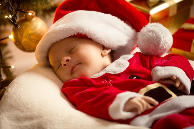 Portrait de bébé garçon en costume de Père Noël couché sous l'arbre de Noël. Notion de Noël