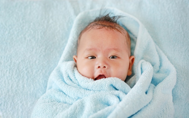 Portrait de bébé garçon en rouleau de serviette en regardant la caméra allongée sur le lit après le bain.