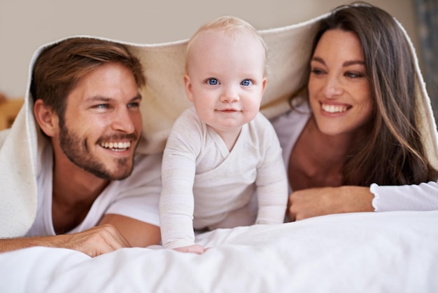 Portrait de bébé heureux mère et père avec une couverture dans la chambre pour des soins d'amour et du temps de qualité ensemble Parents amusants nouveau-né enfant et famille se détendre avec une literie fort sourire et à la maison