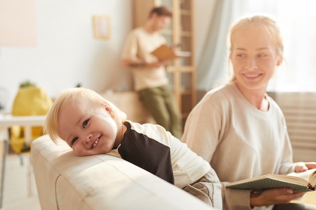 Portrait de bébé heureux souriant tandis que sa mère lisant un livre pour lui sur un canapé dans le salon