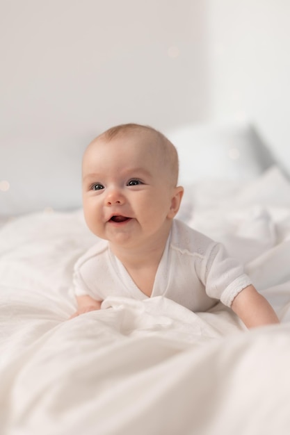 portrait d'un bébé mignon dans un body blanc sur un lit à la maison avec des draps blancs. Bébé nouveau-né à la maison