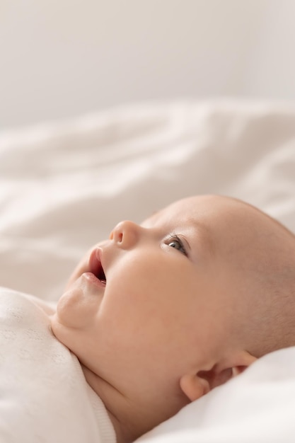 portrait d'un bébé mignon dans un body blanc sur un lit à la maison avec des draps blancs. Bébé nouveau-né à la maison